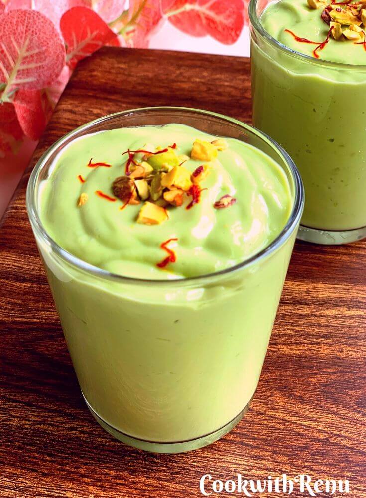 A glass full of thick, creamy and green colour, Indian Style Avocado Lassi, garnished with chopped pistachio and saffron strands