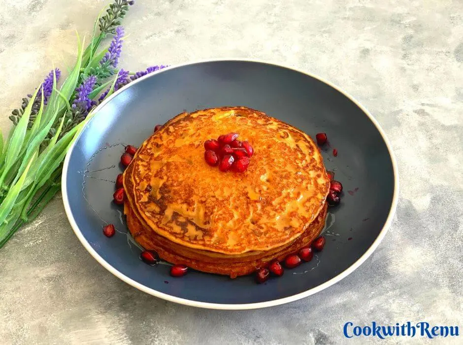 Buckwheat Sweet Potato Pancakes, layered one above the other with a drizzle of maple syrup and garnished with pomegranate