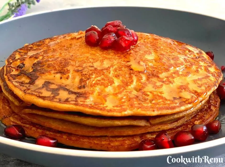 Buckwheat Sweet Potato Pancakes, layered one above the other with a drizzle of maple syrup and garnished with pomegranate