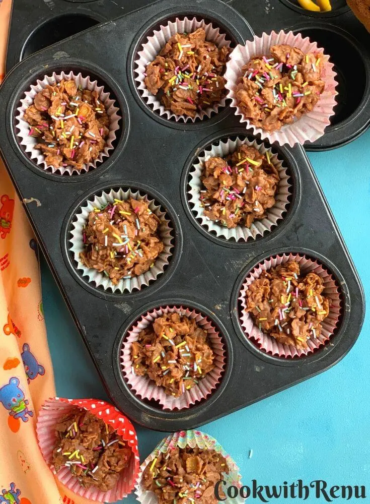 Crunchy Chocolate Cornflakes arranged in a muffin tray and few on top. They are served with sprinklers on top