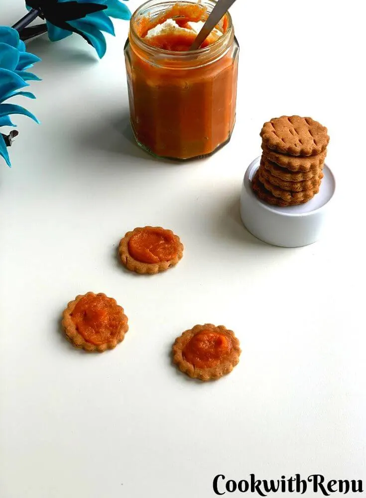 Lehsun Chutney being spread on three baked matri and presented in a glass jar. There is also a stack of baked matri on a bowl