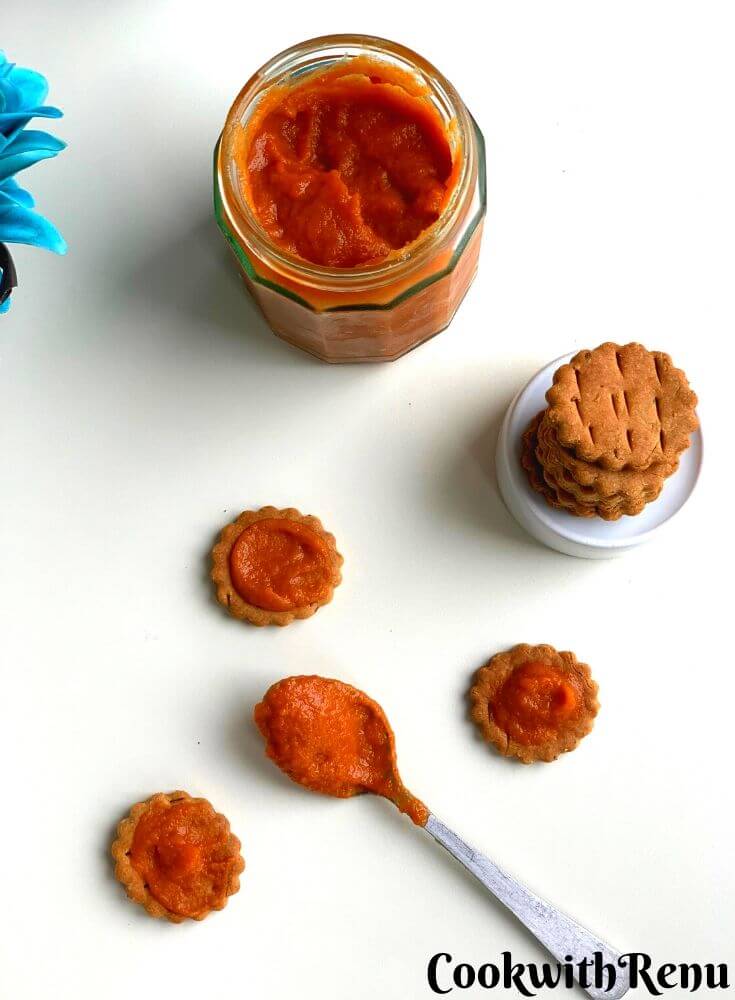 Lasoon Chutney being spread on three baked matri and presented in a glass jar. A spoonful with Lehsun chutney lies in the centre. There is also a stack of baked matri on a bowl