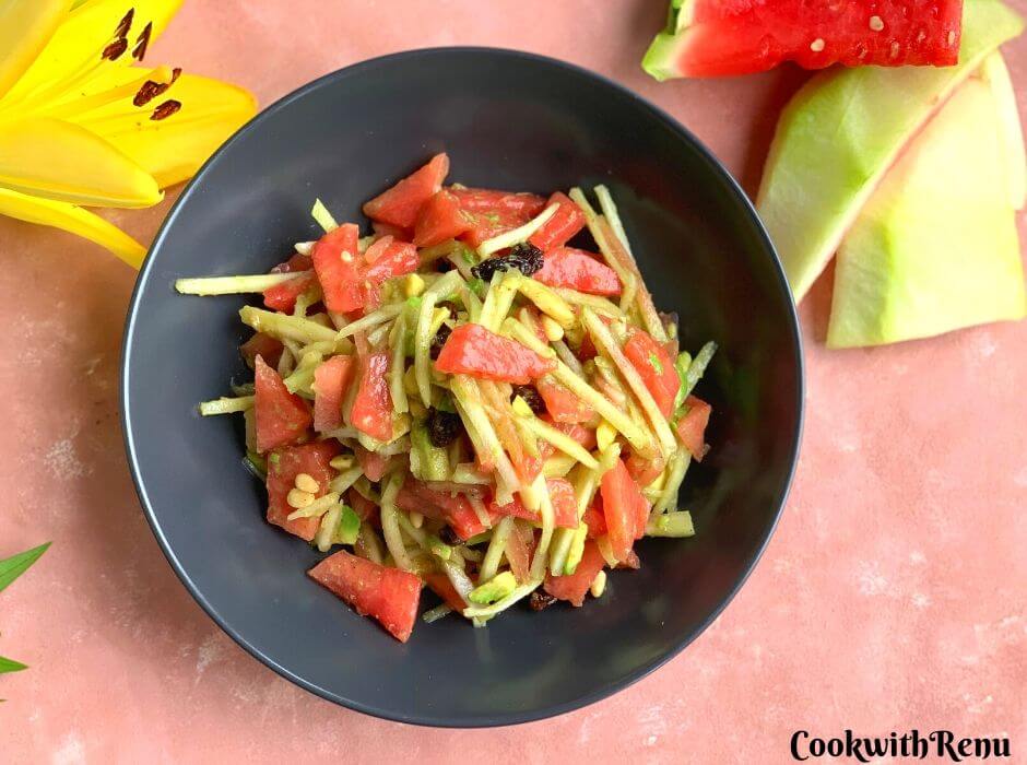 Raw Watermelon Rind and Avocado Salad seen in the pic in a black bowl. Few pieces of watermelon slices are seen in the background and a yellow lily flower for presentation.