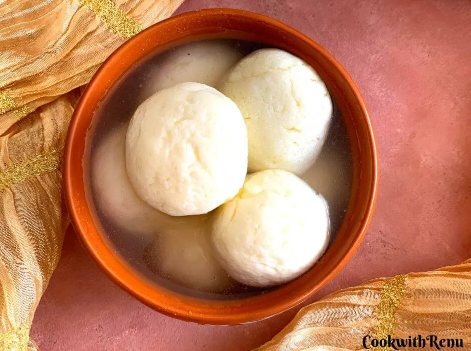 A little closer look of rasgulla presented in a brown bowl, with a golden stole on the side