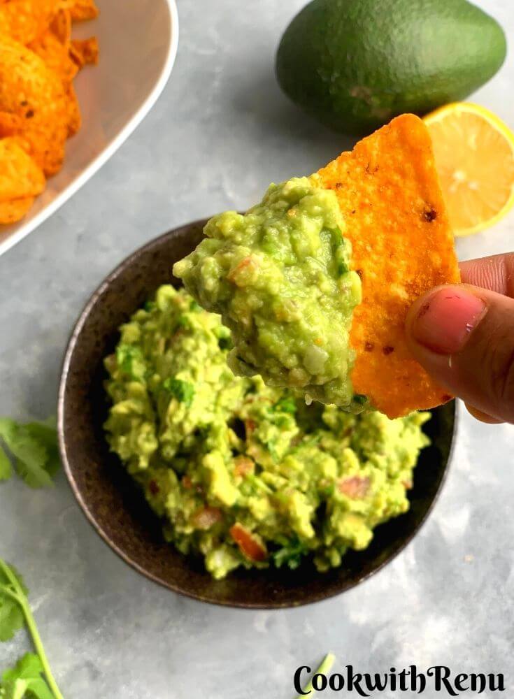 Nacho spread with Guacamole seen in close up. Avocado and lemon seen in background with a bowl of nachos and Guacamole
