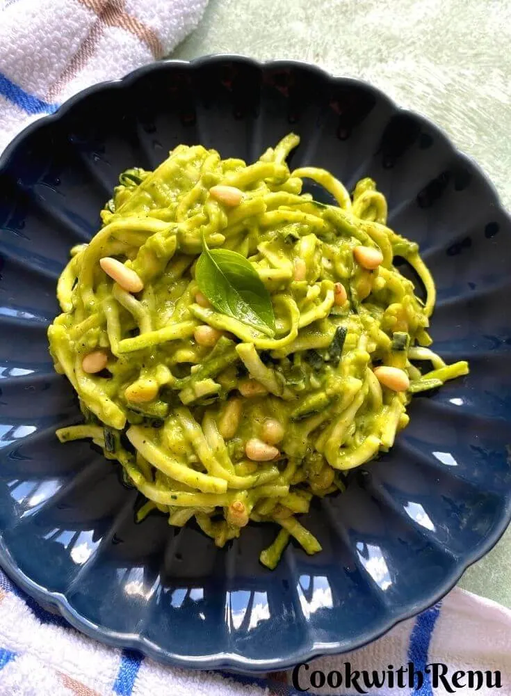 The creamy texture of Zucchini pasta, when more of Avocado Dip is added. The pasta is served in a blue round dish with a kitchen towel around.