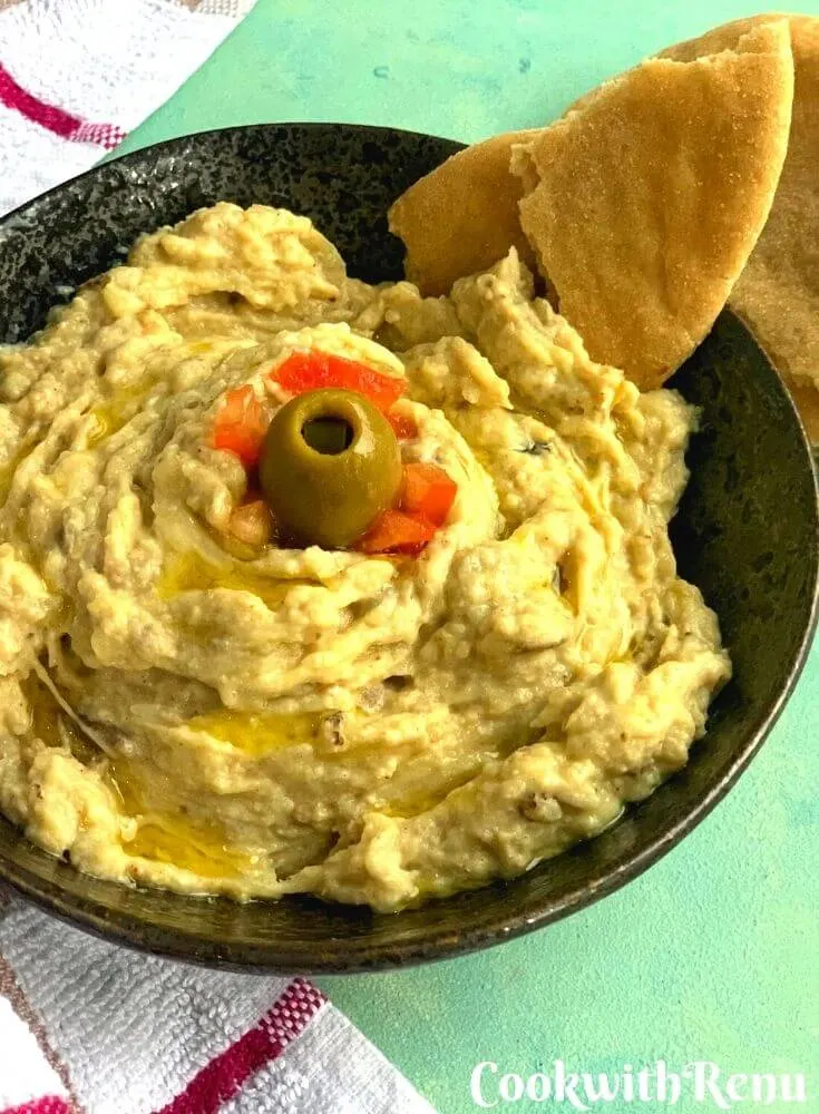 Baba Ghanoush or baba ganoush is a smoky addictive eggplant dip made with mashed and cooked eggplant, tahini, lemon juice, olive oil, & salt. It is served with some pita bread with a garnish of oil, tomato and olives.
