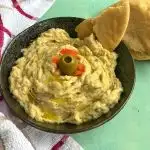 Baba Ghanoush or baba ganoush is a smoky addictive eggplant dip made with mashed and cooked eggplant, tahini, lemon juice, olive oil, & salt. It is served with some pita bread with a garnish of oil, tomato and olives.