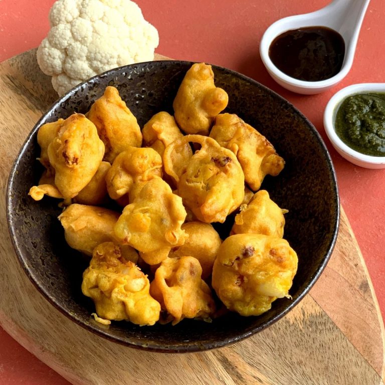 Gobi pakora or Cauliflower pakoda is an irresistible and addictive tea time fritter which are crunchy on the outside, soft inside and perfect as a party appetizer. They are served in a black bowl with 2 chutneys, coriander and tamarind.