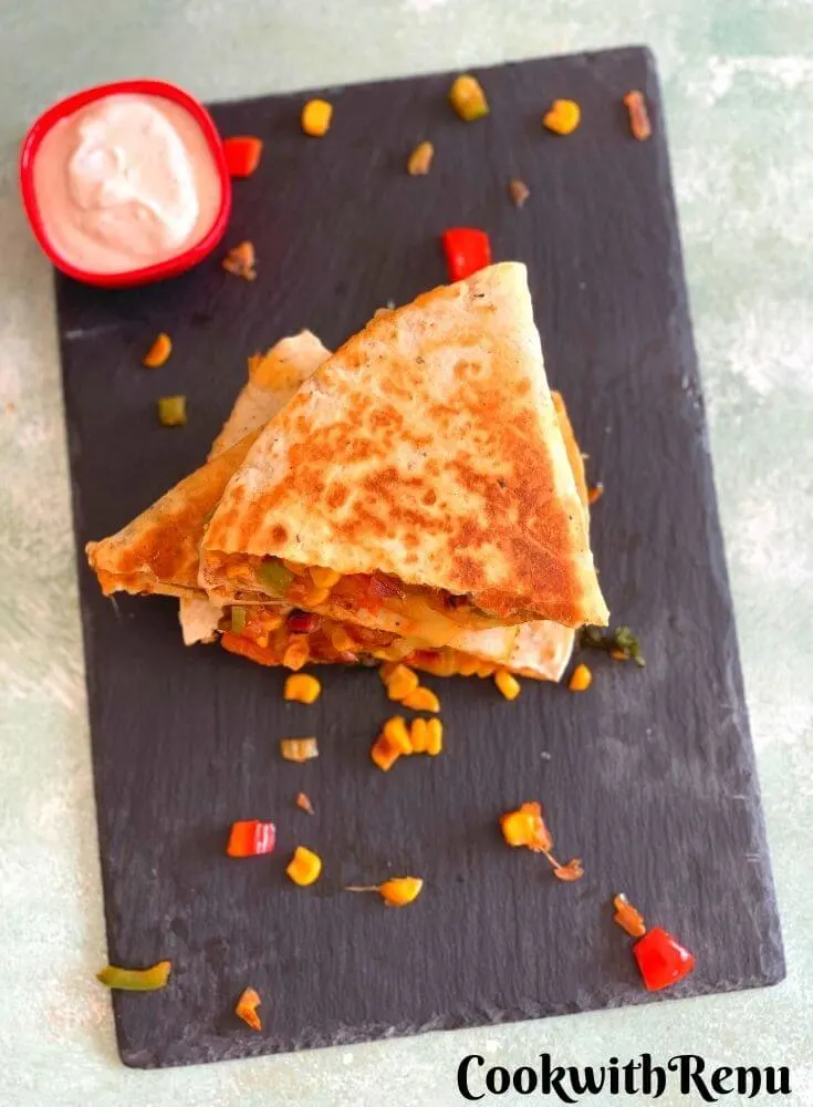 Vegetarian quesadilla arranged on a black serving board with a yogurt dip. They have been stocked one above the other