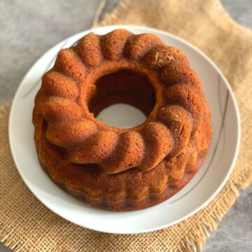 Pumpkin bundt cake on a white plate with a brown jute cloth in the background.