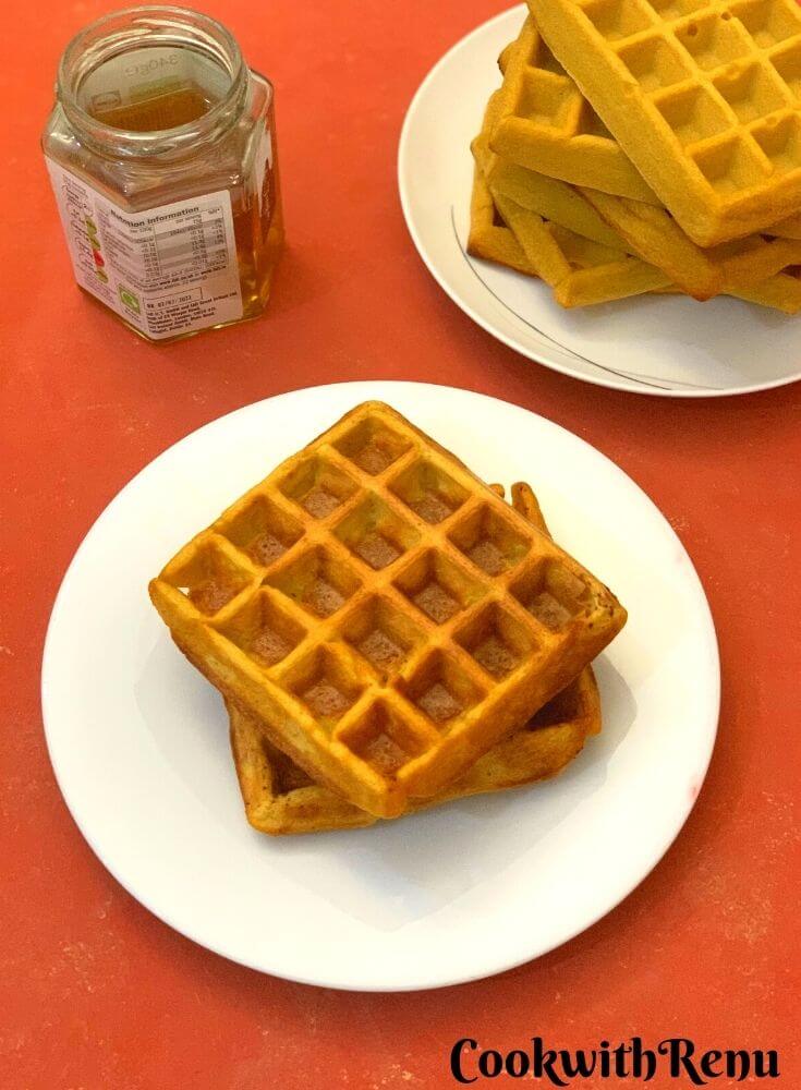 Waffles served in a plate, Honey and a stack of waffles seen on the side.