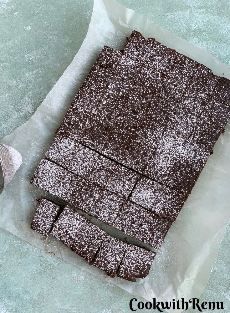 Baked brownie squares on a parchment paper, with a drizzle of icing sugar