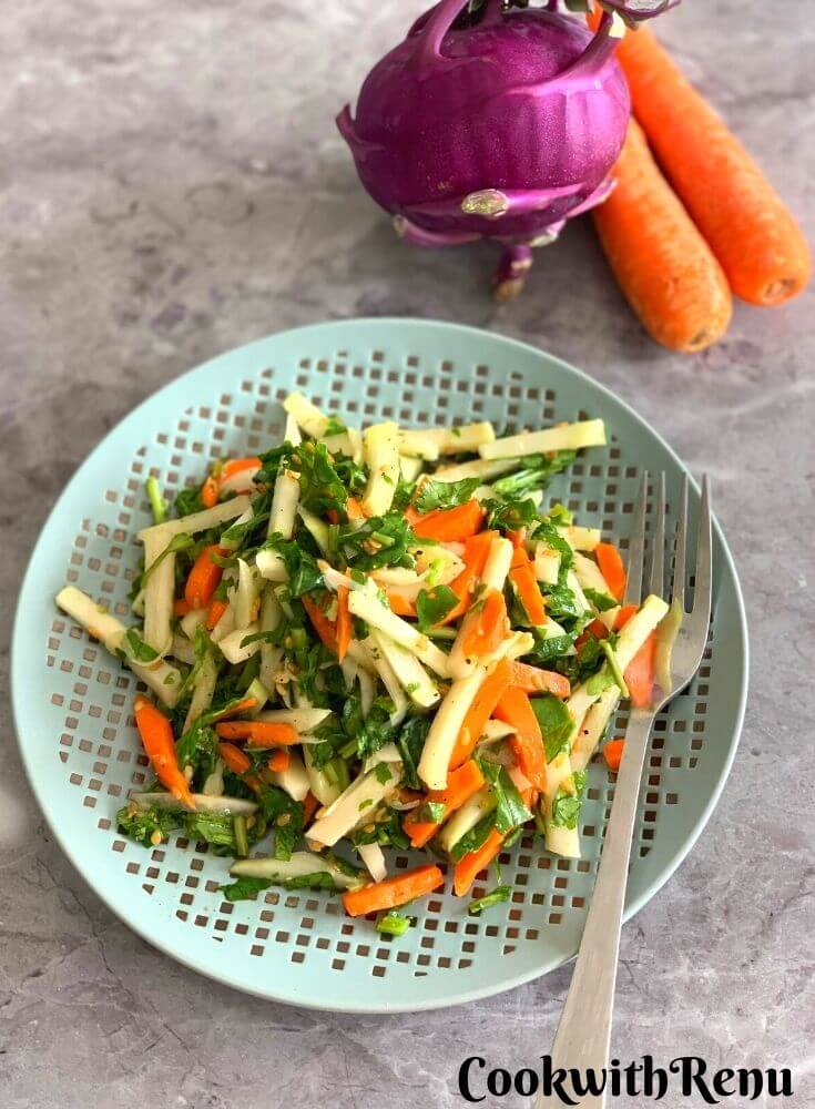 Kohlrabi, Carrot, and Spinach Salad served on a plate. Seen in the background is purple Kohlrabi and carrot