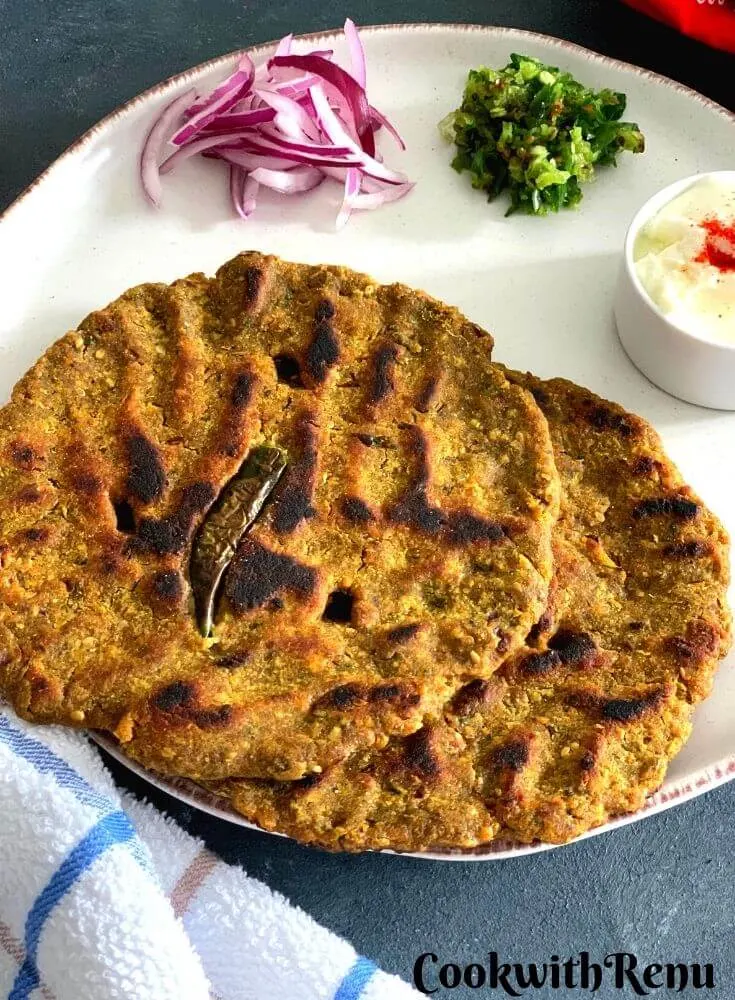 Close up look of Thalipeeth served in a white plate with yogurt, green chilly and onion.
