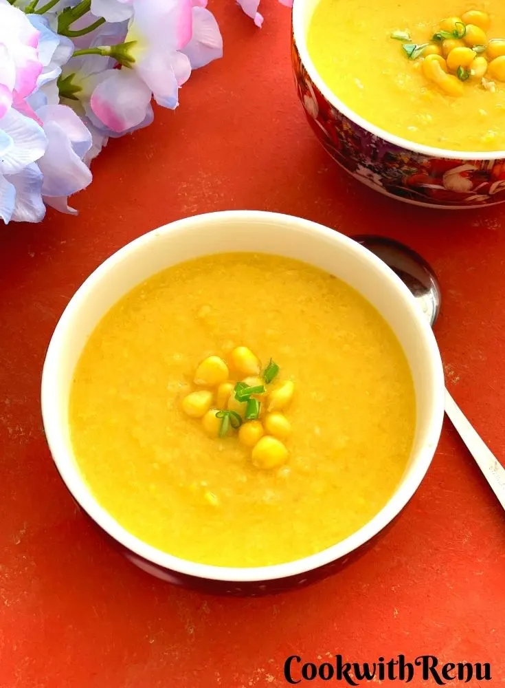 Close up look of Vegan Sweet Corn Soup served in 2 white bowl, garnished with corn kernels and few scallion greens