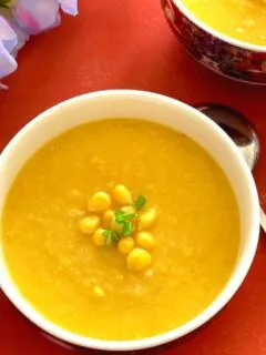 Close up look of Vegan Sweet Corn Soup served in white bowl, garnished with corn kernels and few scallion greens