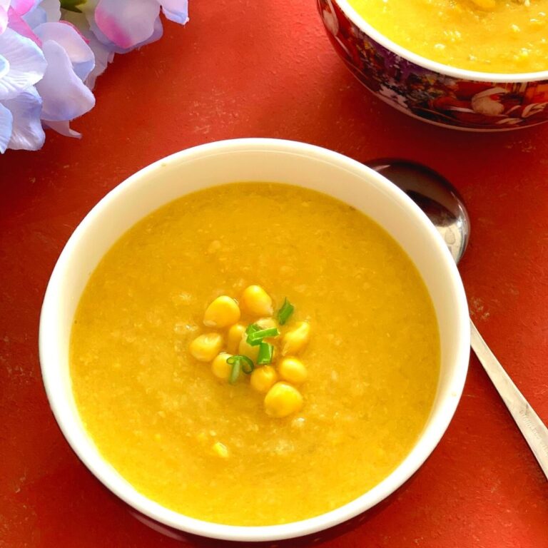 Close up look of Vegan Sweet Corn Soup served in white bowl, garnished with corn kernels and few scallion greens