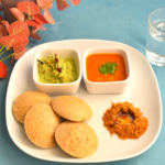 4 Idlis served along with chutney, sambar, podi with ghee on a white plate