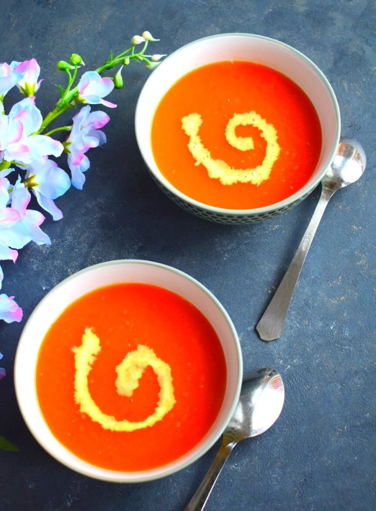 2 Bowls of Soup, with a bit of cream garnish. Seen along side are some artificial flowers