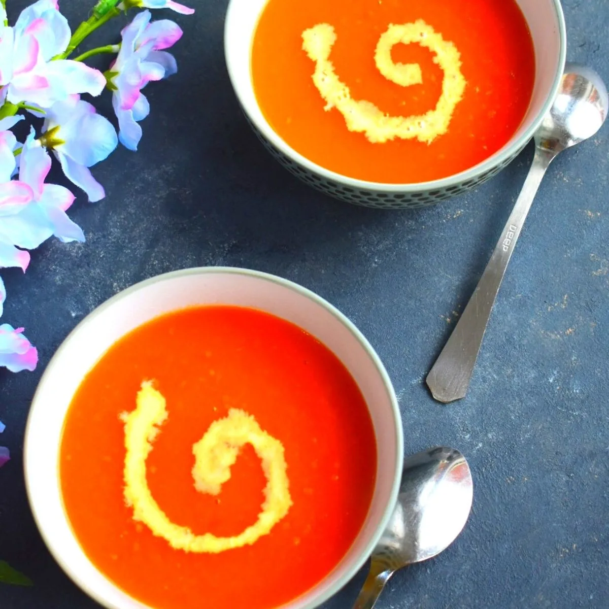 2 Bowls of Soup, with a bit of cream garnish. Seen along side are some artificial flowers