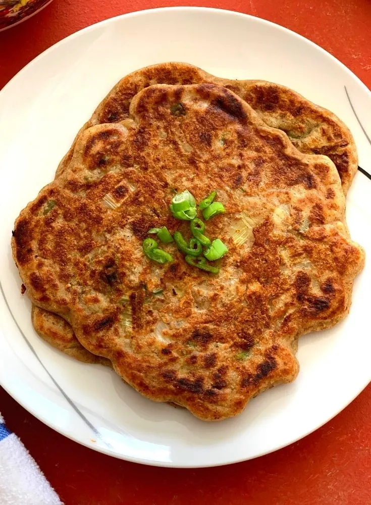 Close up look of pancakes served on a white plate with a bit of garnish of green onions