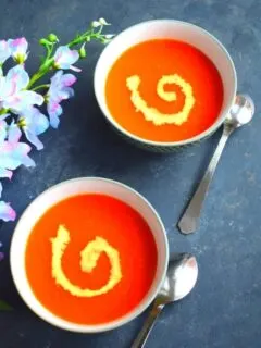 2 Bowls of Soup, with a bit of cream garnish. Seen along side are some artificial flowers