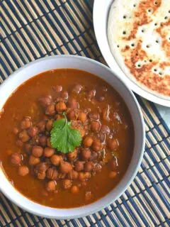 Kala Chana Served in a bowl and seen on a blue brown placemat. Seen along are some amboli served