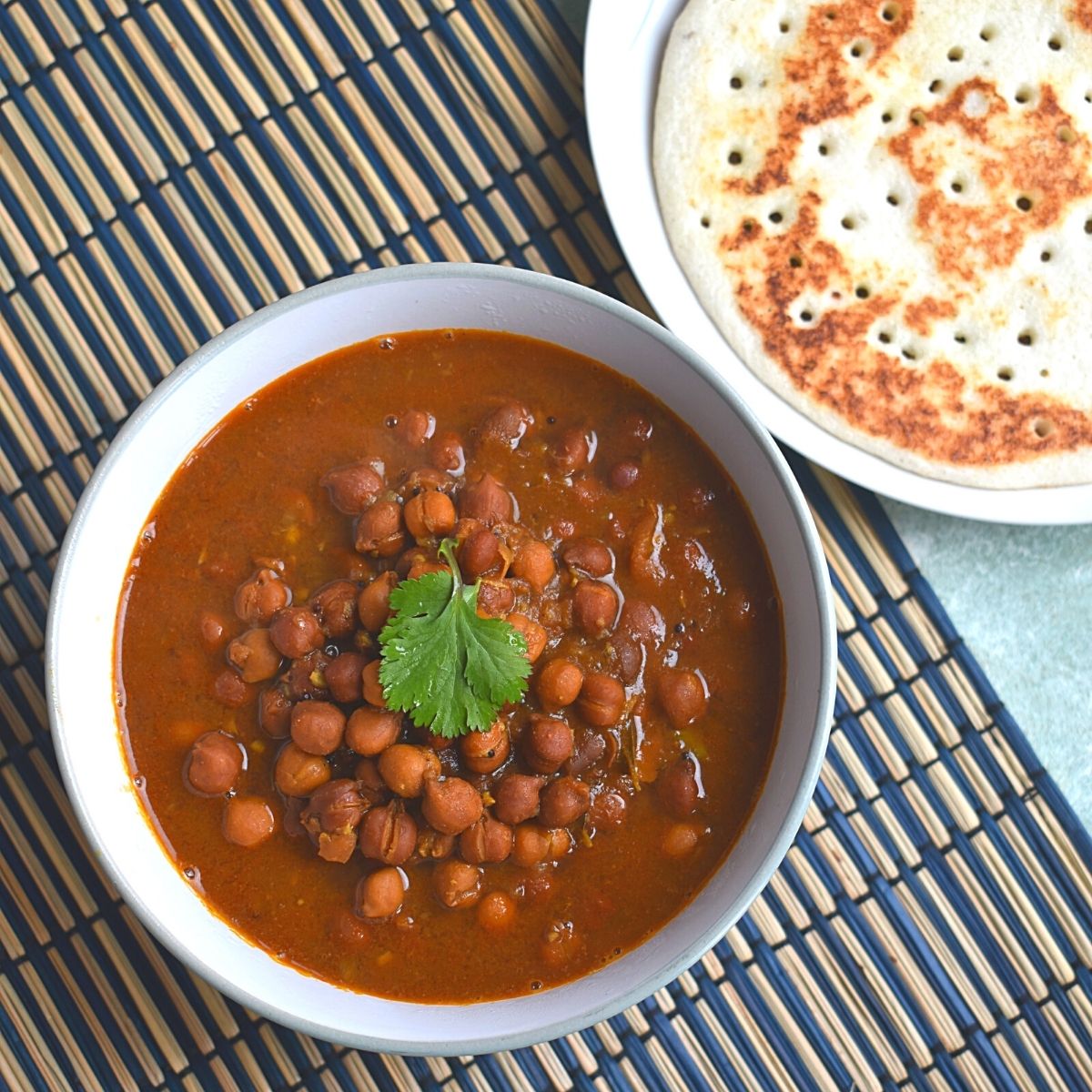 Kala Chana Served in a bowl and seen on a blue brown placemat. Seen along are some amboli served