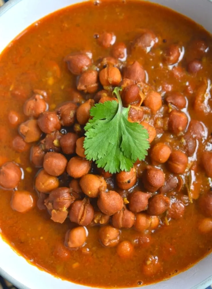 Close up look of Kala Chana Amti served in a bowl with a small coriander leaf on top. The cooked chana is visible perfectly