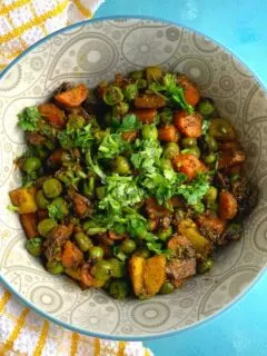 A grey bowl with the sabji and coriander garnished on top. Seen on the side is a yellow kitchen towel