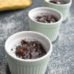 3 Chocolate Instant Pot Mug cakes seen in a line, with a banana on the side. It has a drizzle of white icing sugar