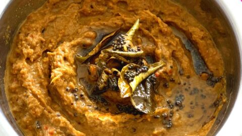 Close up look of celery chutney with a tadka of oil, curry leaves and mustard seeds on top in a steel bowl