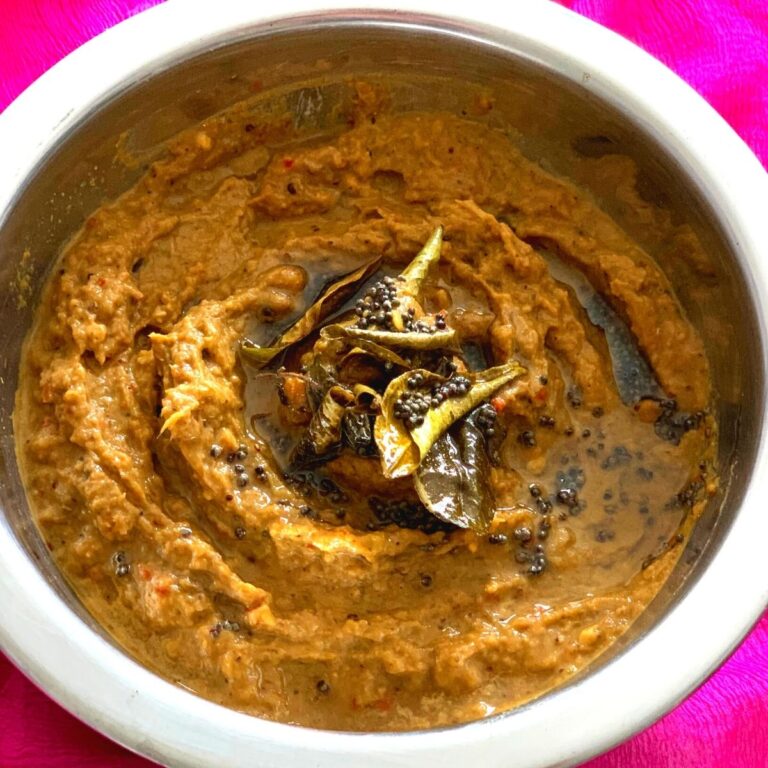 Close up look of celery chutney with a tadka of oil, curry leaves and mustard seeds on top in a steel bowl