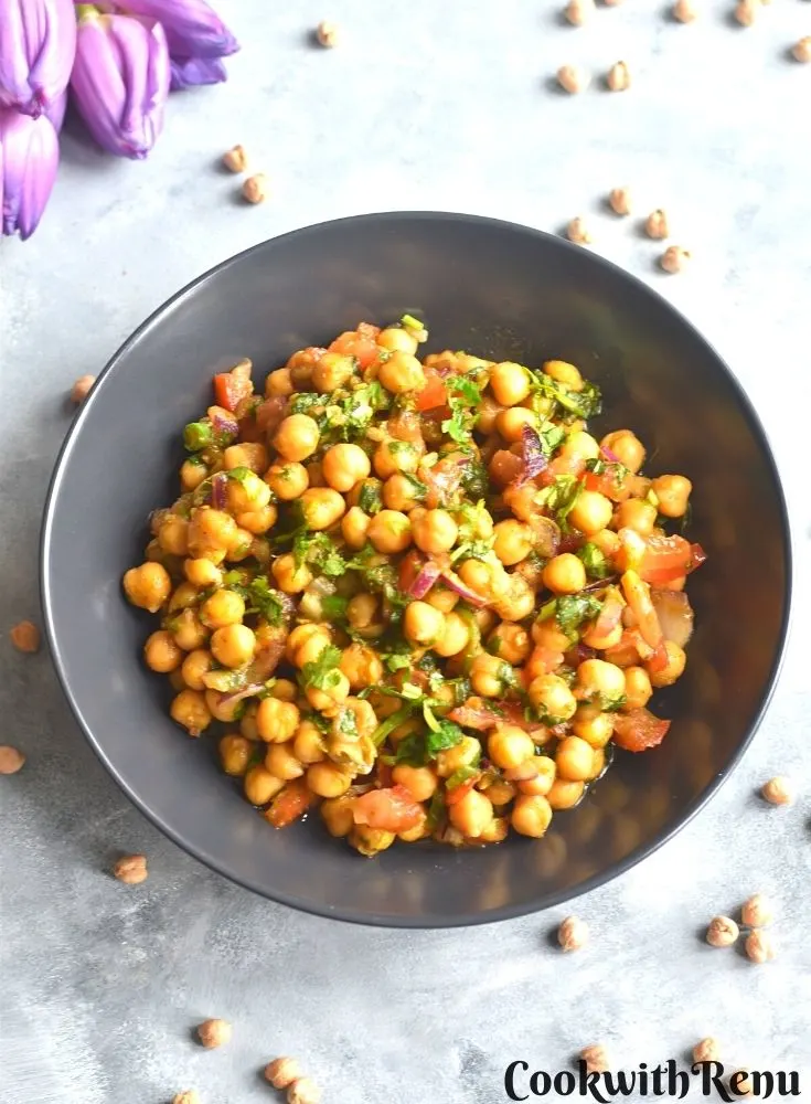 Chickpea salad served in a black bowl, with some chickpeas seen scattered with some tulips seen in the background