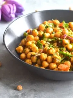 Close up look of Chickpea salad served in a black bowl, with some chickpeas seen scattered with some tulips seen in the background