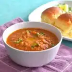 Pav Bhaji being served in a white bowl. Seen along side are some pav.