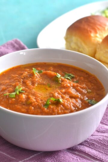 Pav Bhaji being served in a white bowl. Seen along side are some pav.