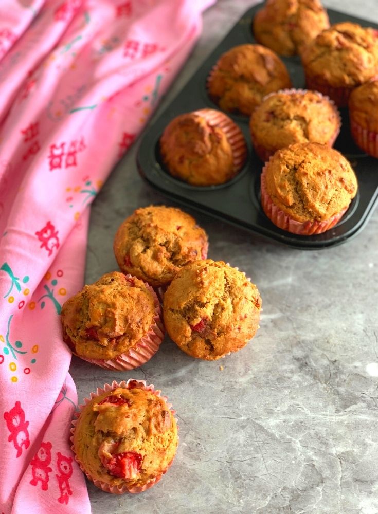 Eggless Strawberry Muffins seen on a muffin tray as well as on a table with a stole beside it