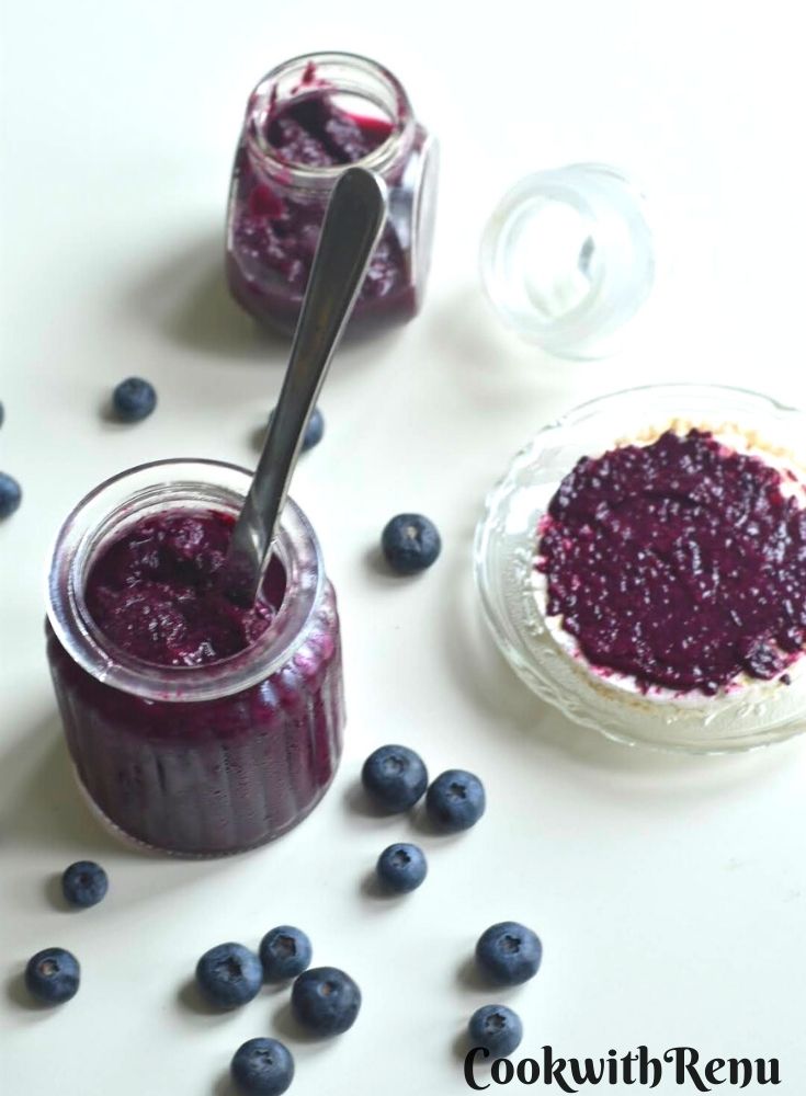 Blueberry chia jam spread on a rice cracker. Seen are 2 bottles of jar filled with jam along with some berries spread across.