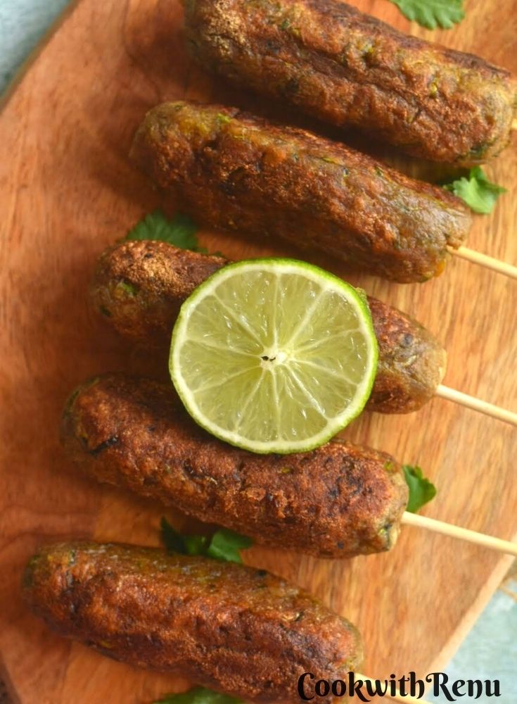 Close up look of Kacche kele ke kebab arranged on a wooden board with a garnish of lemon.