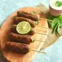 Farali Raw Banana Kebab arranged on a wooden board with a garnish of lemon. Seen along side is a dip served along with chillies