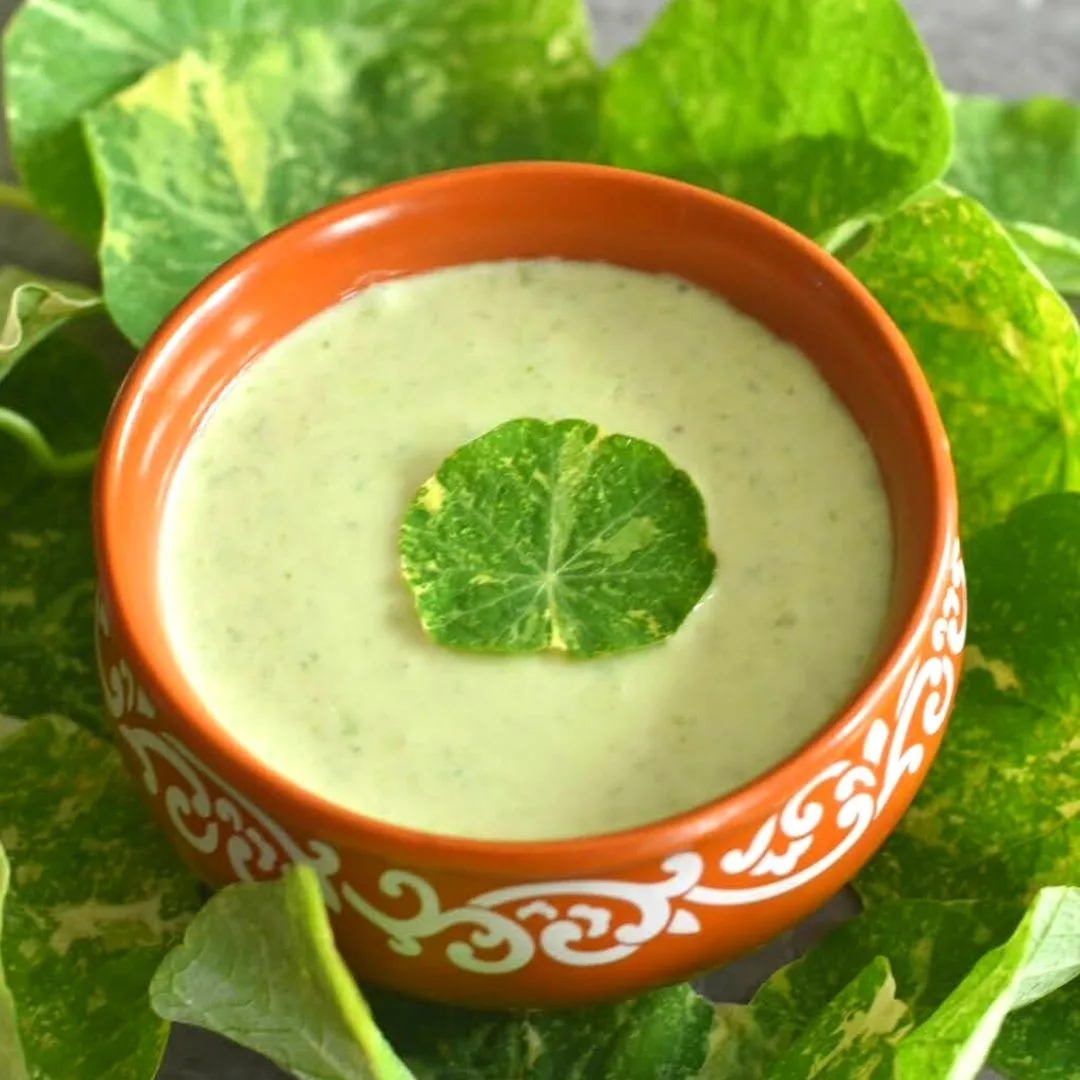 Nasturtium Leaves & Stems Raita served in a brown bowl with some leaves scattered around
