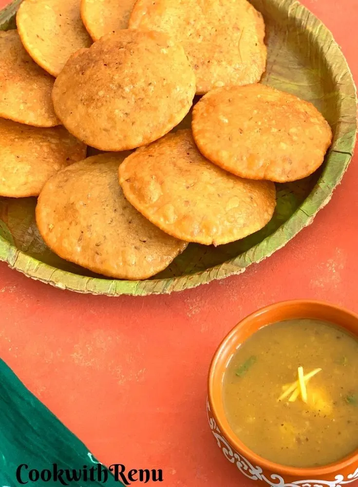 A plate served with crispy bedais. Seen in the background is a bowl of aloo saag