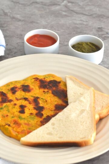 Vegan Chickpea Tomato Omeletee served with a bread slice along with tomato ketchup and green coriander chutney