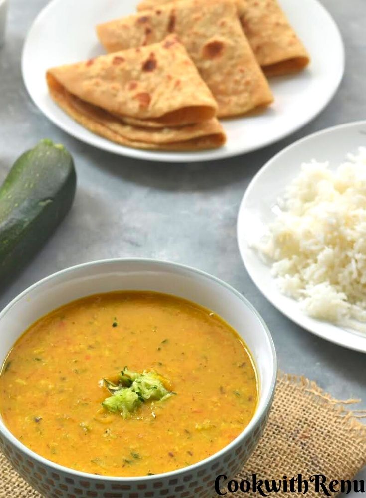 Zucchini dal served in a white bowl along with hot steaming white rice and some roti