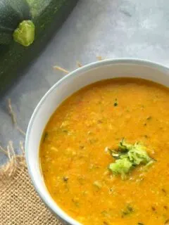 Zucchini Tomato Dal Served in a white bowl. Seen along side are some fresh zucchini.