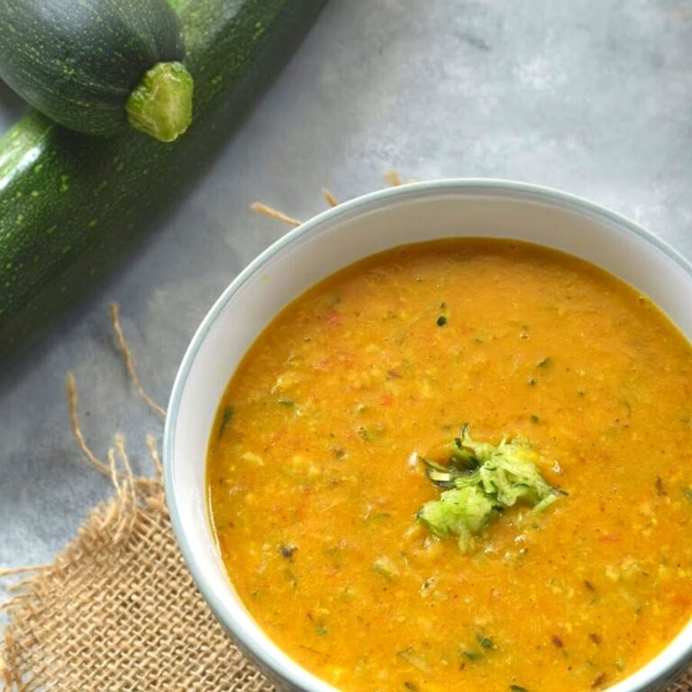 Zucchini Tomato Dal Served in a white bowl. Seen along side are some fresh zucchini.