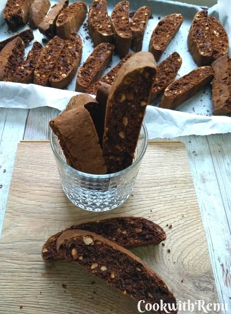 Twice baked Biscotti showcased in a glass and a wooden board. Seen in the background are some more on a baking tray