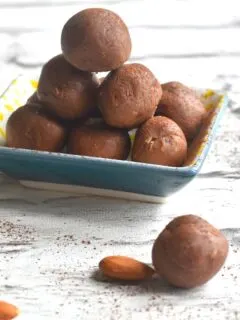 A stack of Milk powder chocolate ladoo arranged on a rectangular plate with a garnish of cocoa powder. Seen along are some almonds scattered.